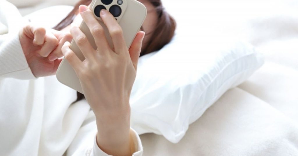 スマートフォンで北海道の紅葉の見頃時期を調べる女性