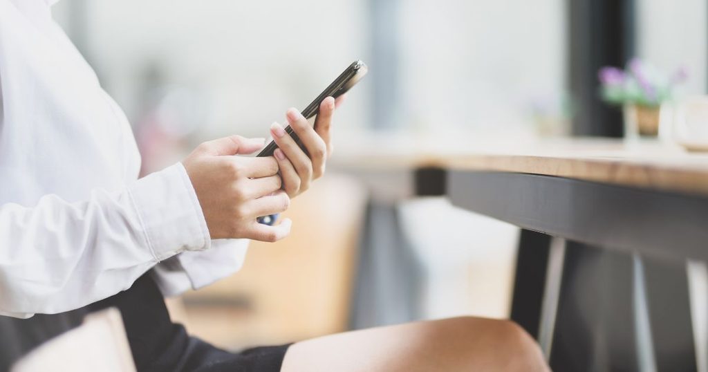 スマートフォンで新潟の紅葉の見頃時期を調べる女性